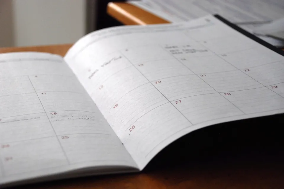 An open paper calendar lying on a wooden desk
