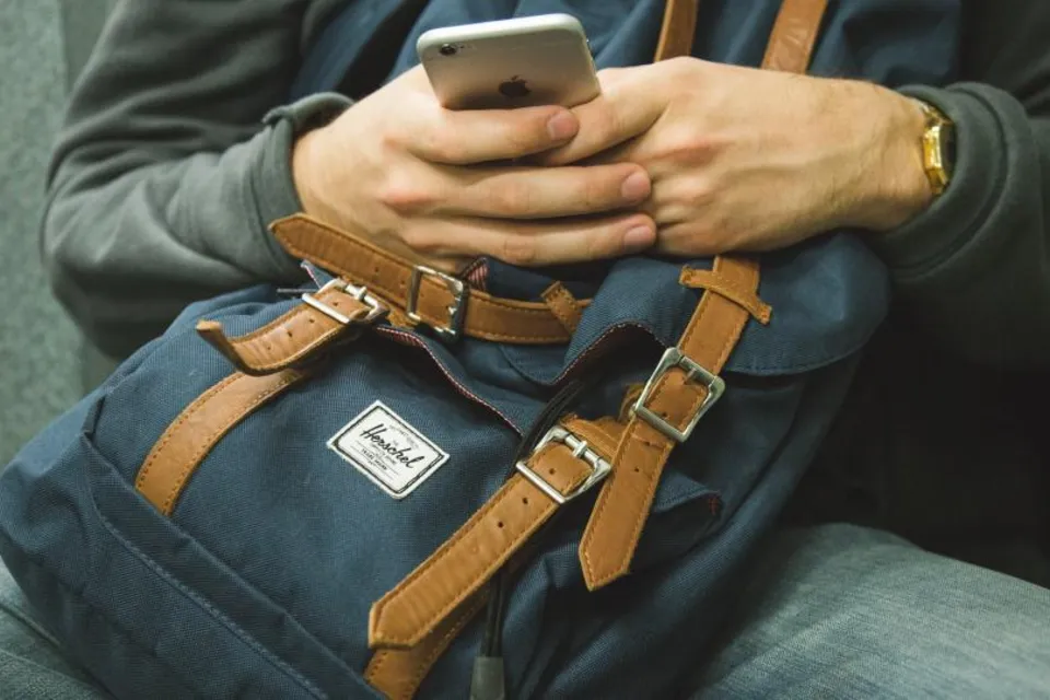 Someone on the move reads on a phone, a backpack on their lap