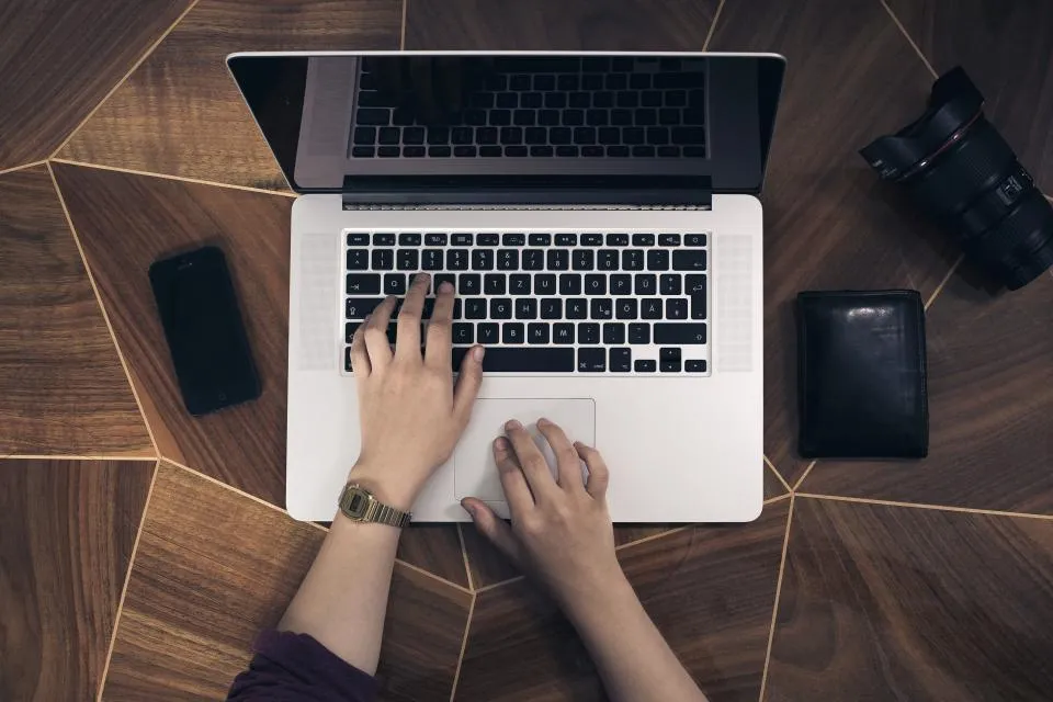 Hands typing on a laptop on a wooden desk